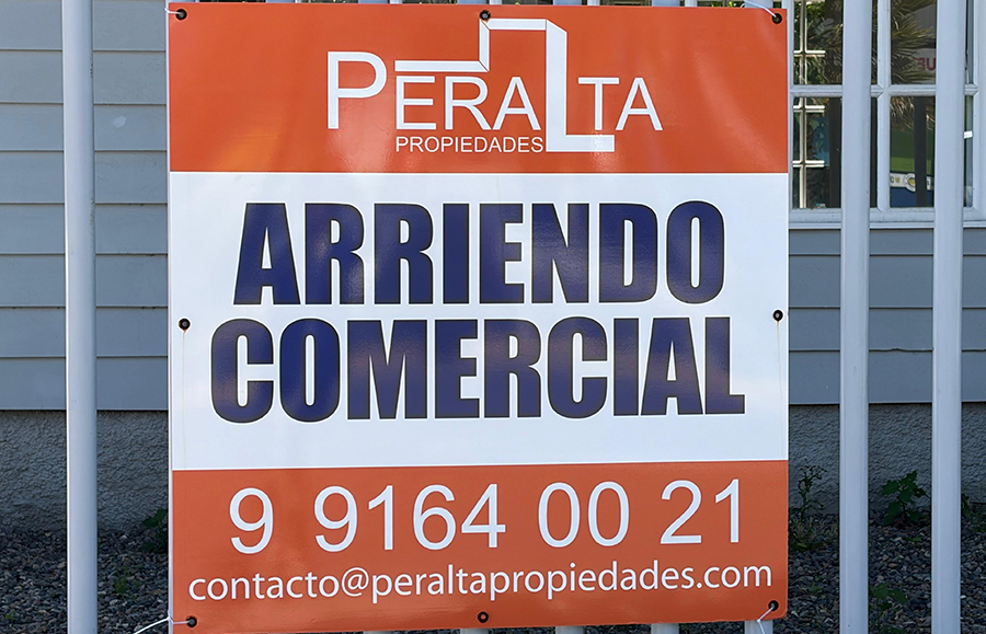 Letrero naranja y blanco de Peralta Propiedades con la leyenda Arriendo Comercial, fijado a una reja blanca